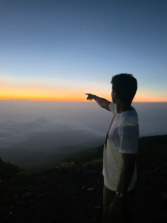 Arun pointing toward the horizon above the clouds at sunrise